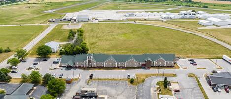 An airport hotel with a large parking lot, multiple buildings, and green fields in the background.