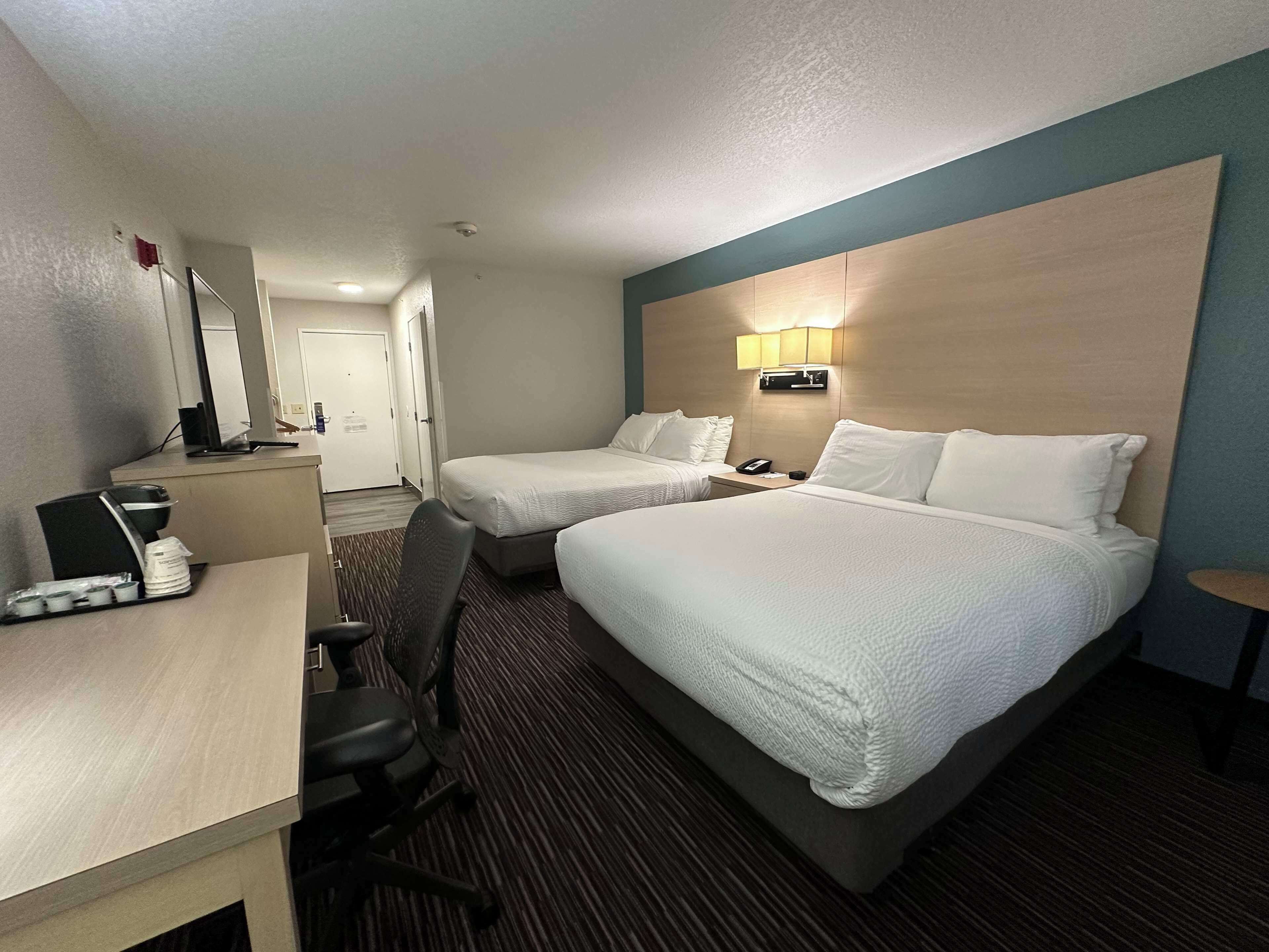 Ein Hotelzimmer mit zwei Betten, einem Schreibtisch mit Computer, einem Stuhl und einem kleinen Tisch mit Lampe.