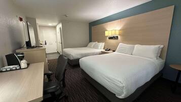 A hotel room with two beds, a desk with a computer, a chair, and a small table with a lamp.