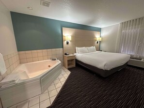 A hotel room with a large bed, a separate bathroom with a bathtub, and a window with curtains.