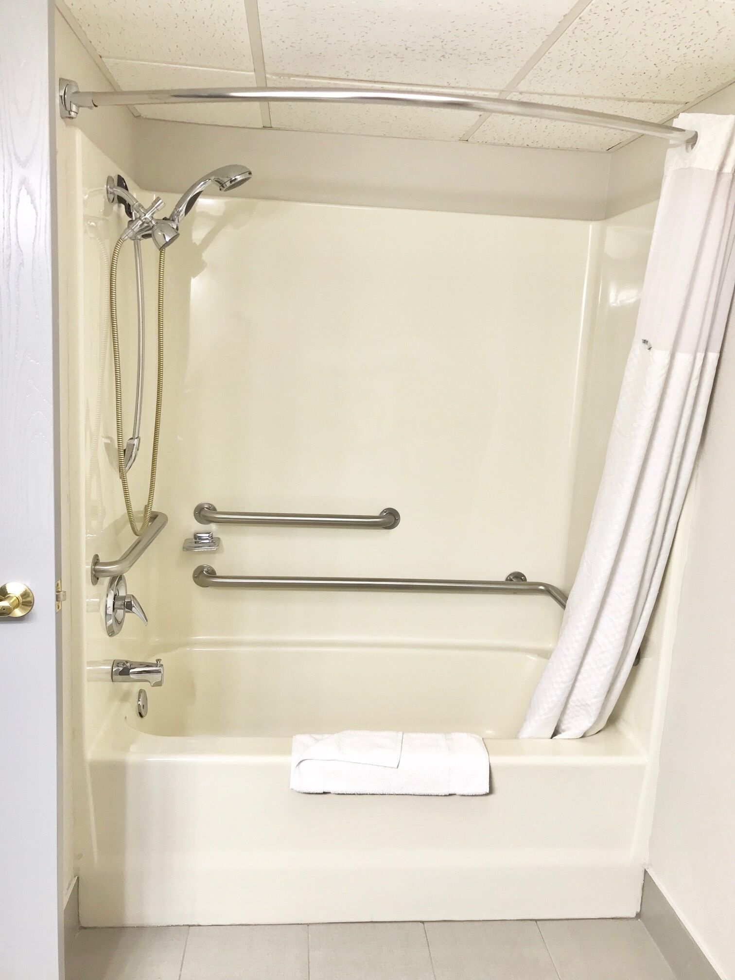 Una vasca da bagno con soffione doccia, maniglie di sostegno e un asciugamano.