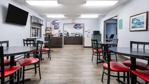 Un restaurante con zona de cocina, mesas con sillas rojas y un televisor de pantalla plana en la pared.