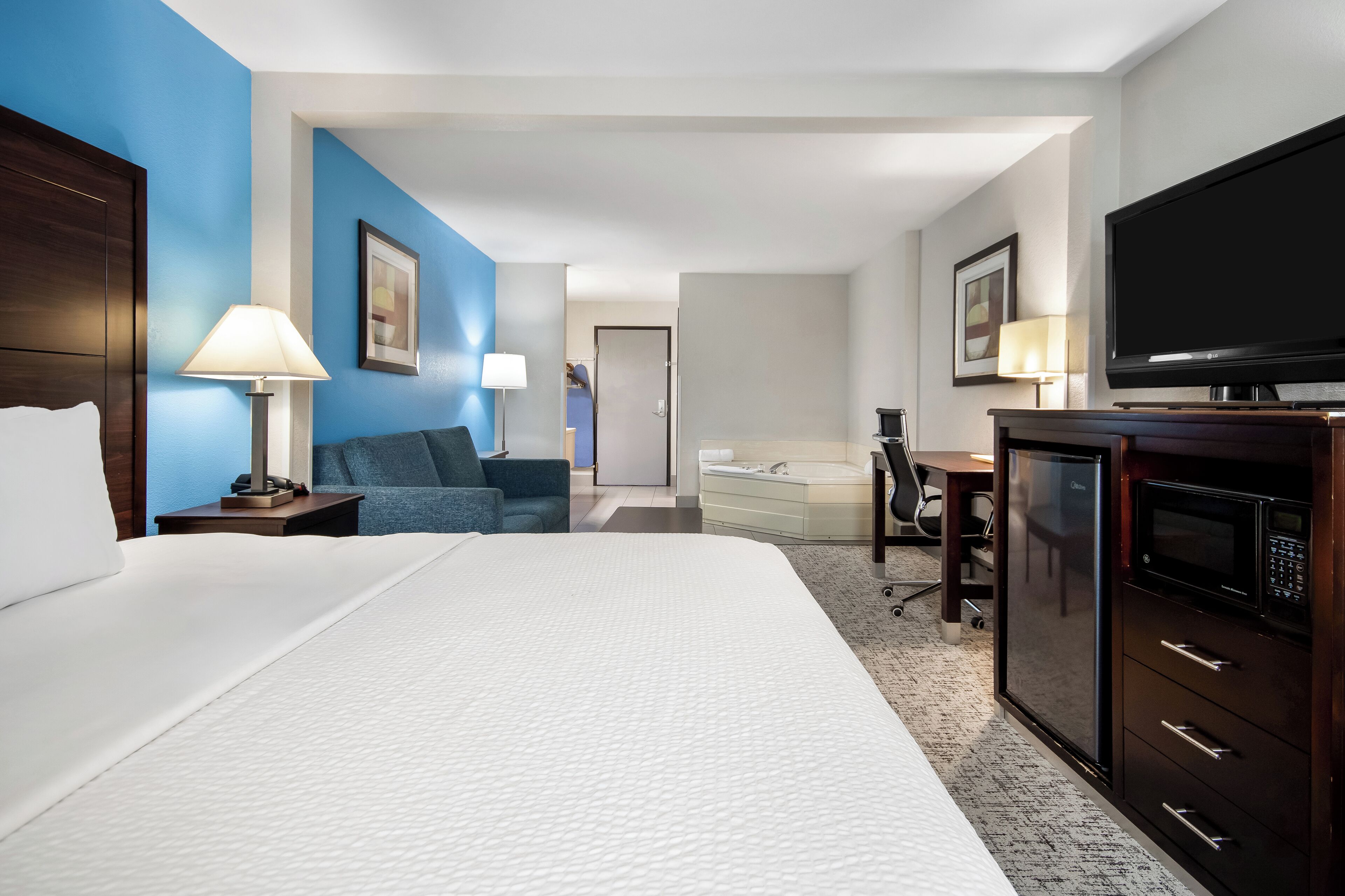 A hotel room with a large bed, a desk with a computer, a television, and a minibar.