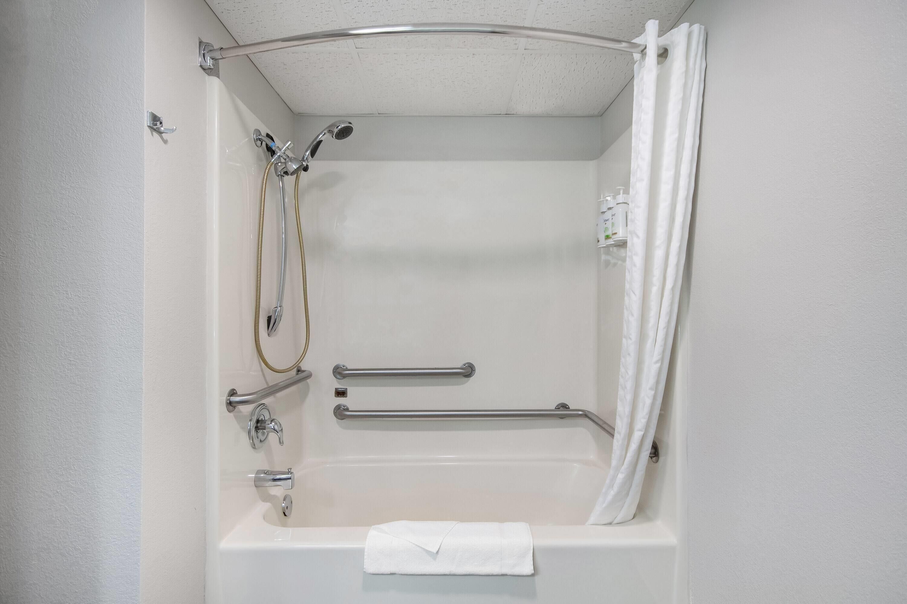 A white bathtub with a shower head, grab bars, and a towel hanging on the side.