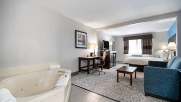 A hotel room with a bathtub, a desk with a chair, a sofa, and a bed.