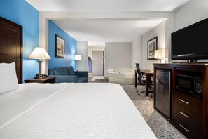 Una habitación de hotel con una cama grande, un escritorio, un televisor y un microondas.