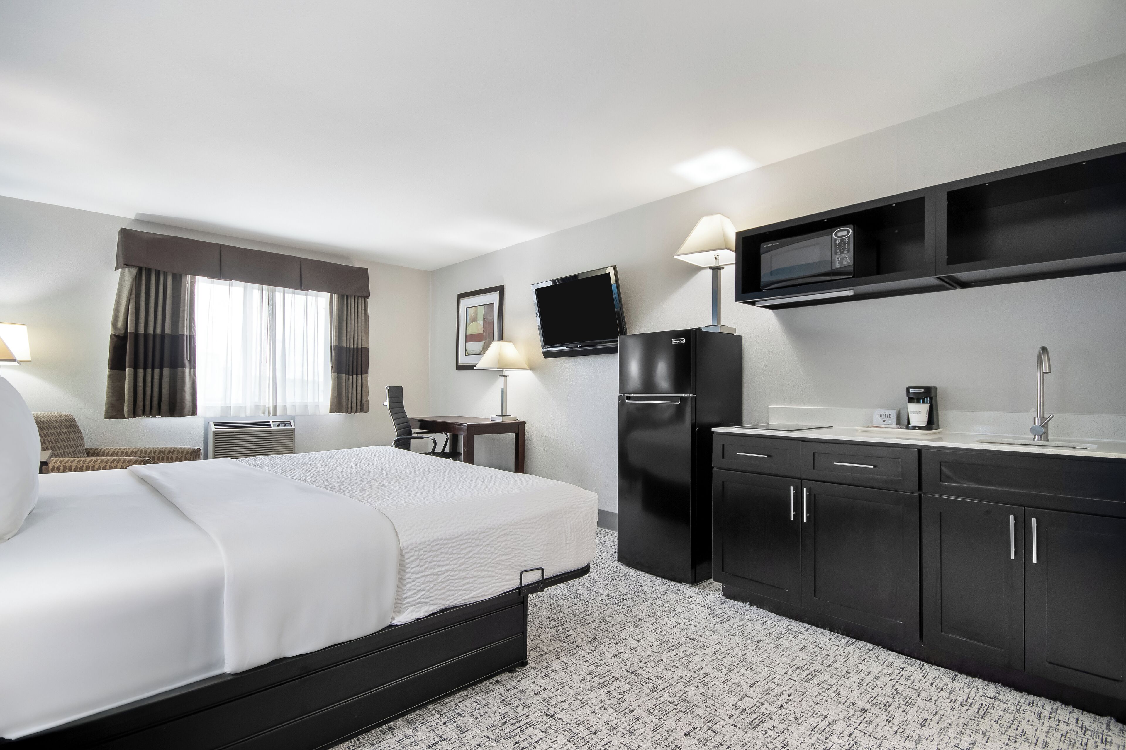 Quarto de hotel com uma cama, uma escrivaninha, um frigorífico, um micro-ondas e uma pia.