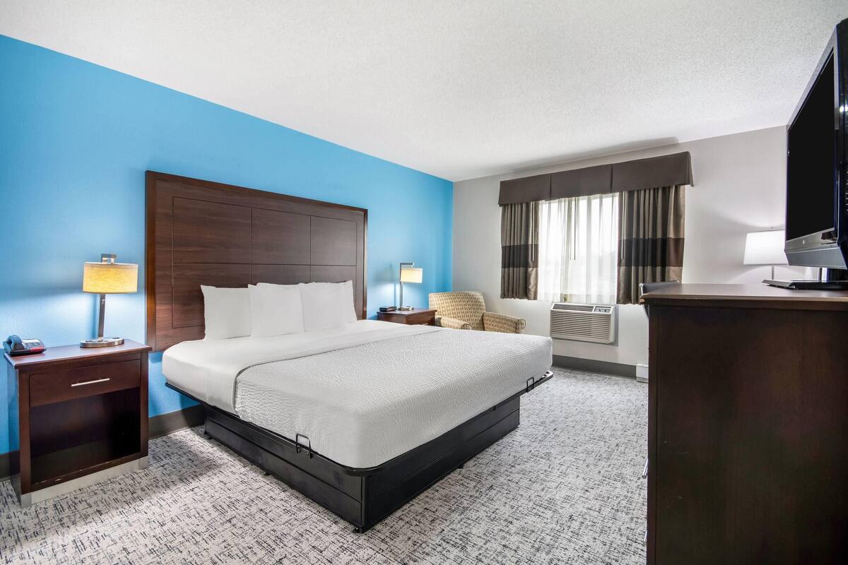 Een hotelkamer met een groot bed, een bureau, een stoel, een televisie en een raam met gordijnen.