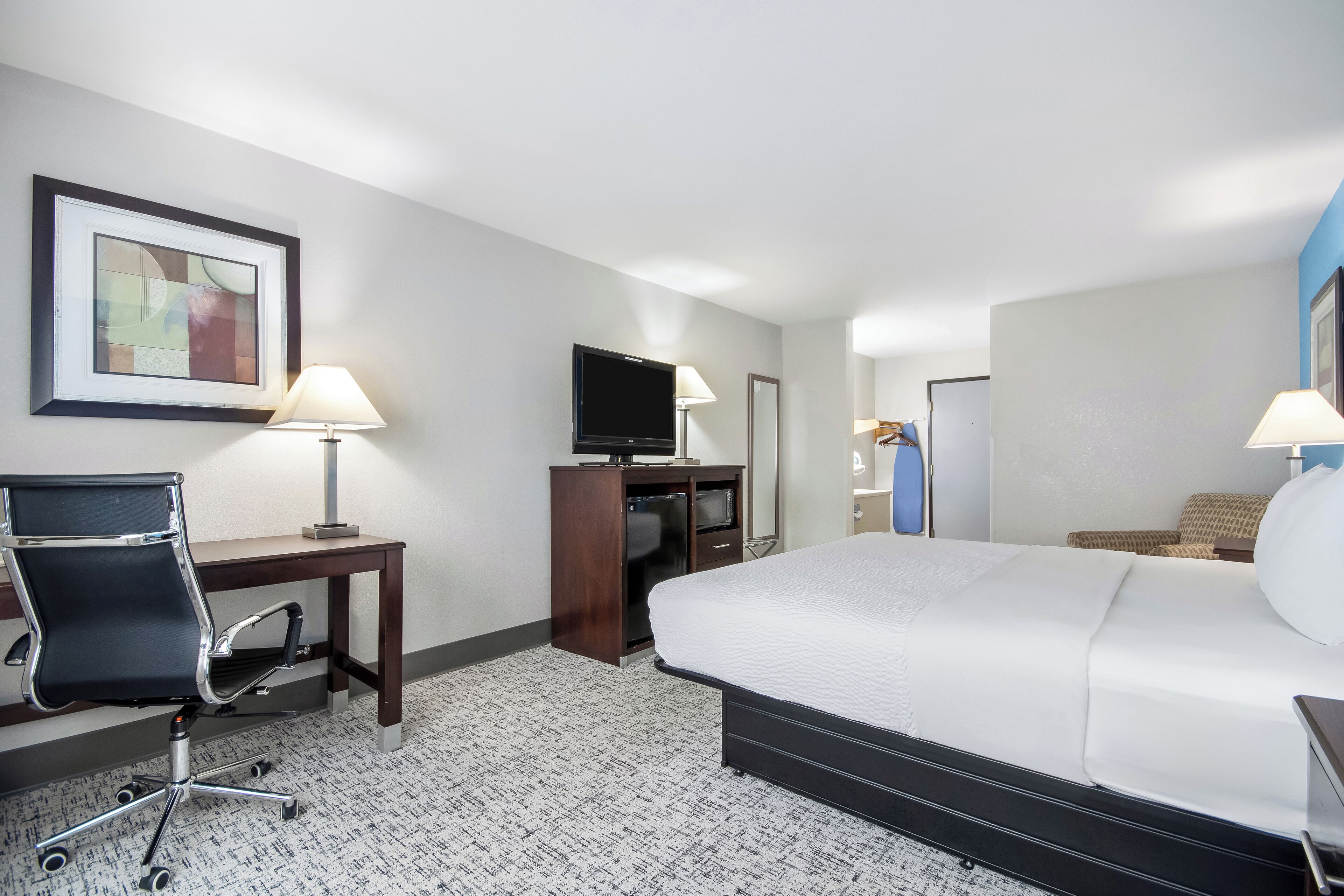 Une chambre d’hôtel avec un lit, un bureau, une chaise, une télévision et un tableau encadré au mur.
