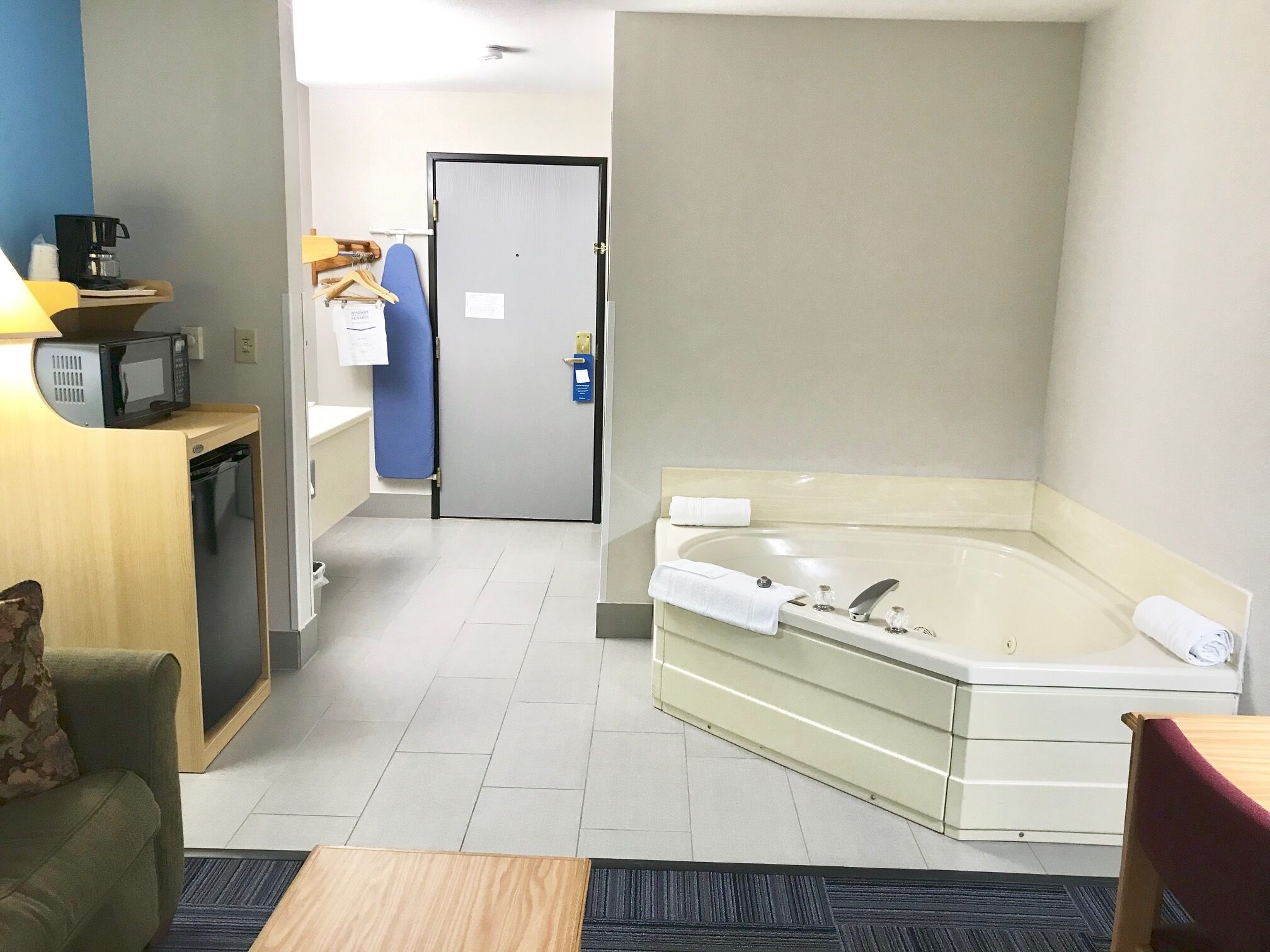 A hotel room with a kitchenette, a large bathtub, a sofa, and a small table.