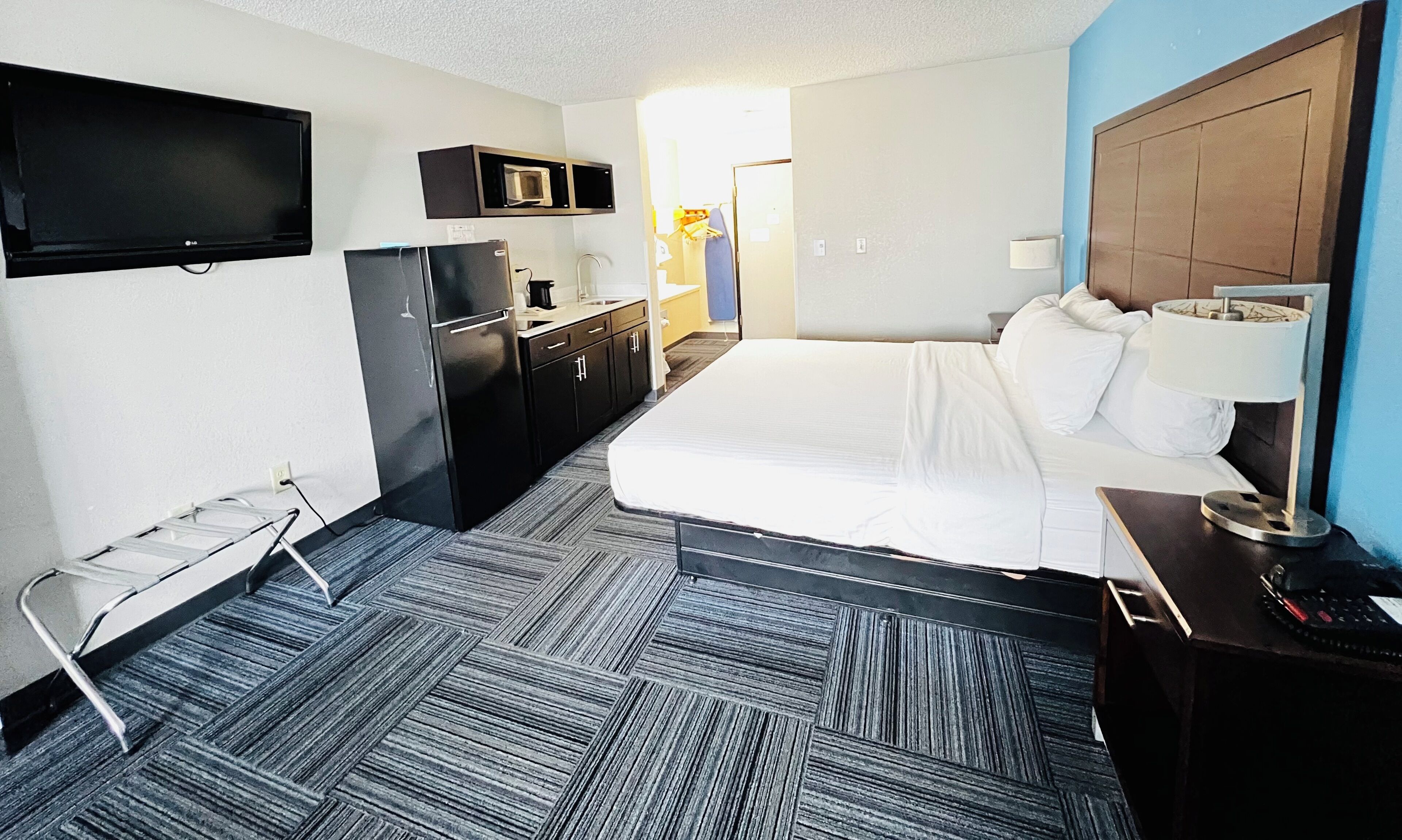 A hotel room with a bed, a desk with a lamp, a refrigerator, a microwave, and a television on the wall.