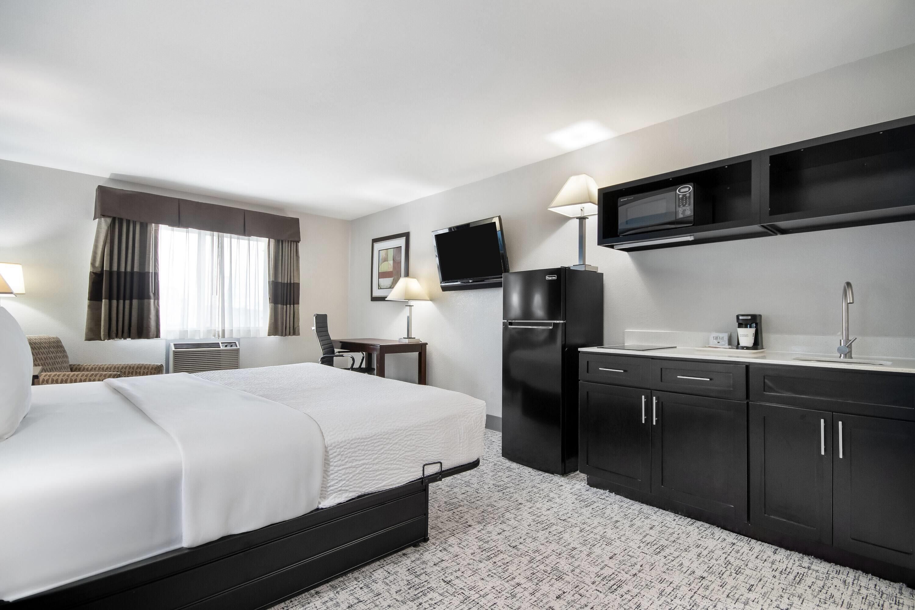 A hotel room with a bed, a desk, a microwave, a refrigerator, and a TV.