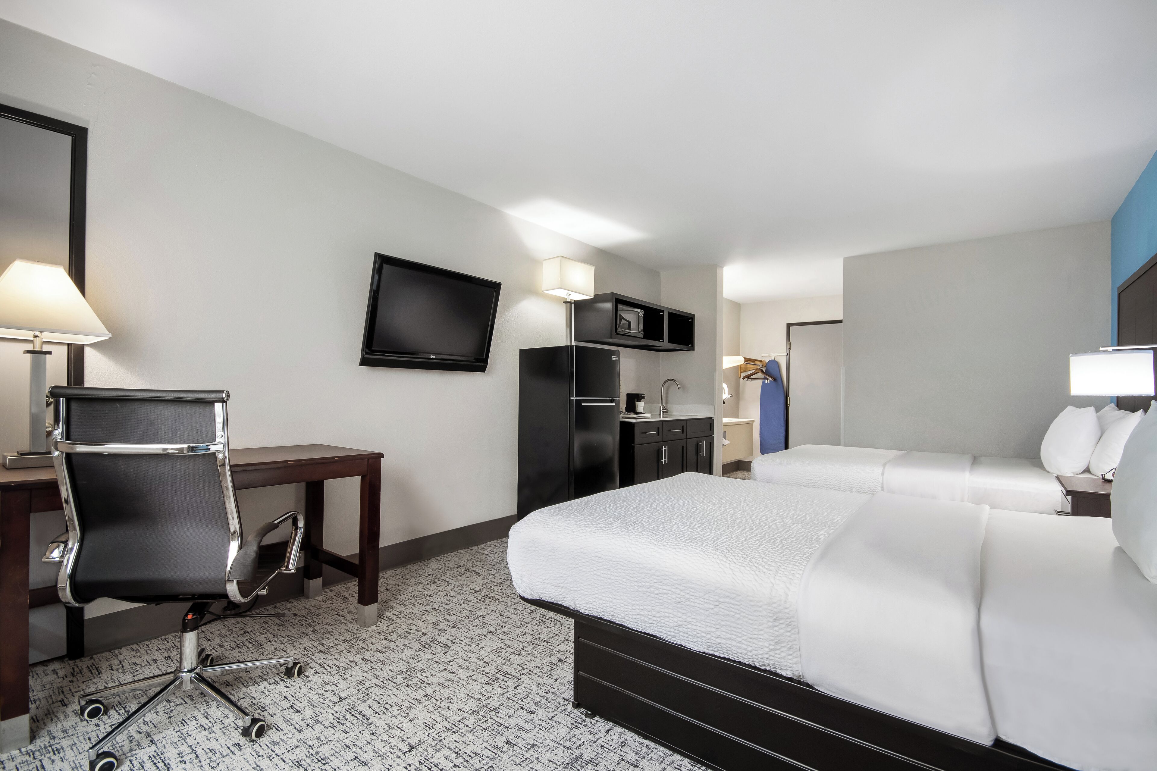 A hotel room with a bed, desk, chair, TV, and a minibar.