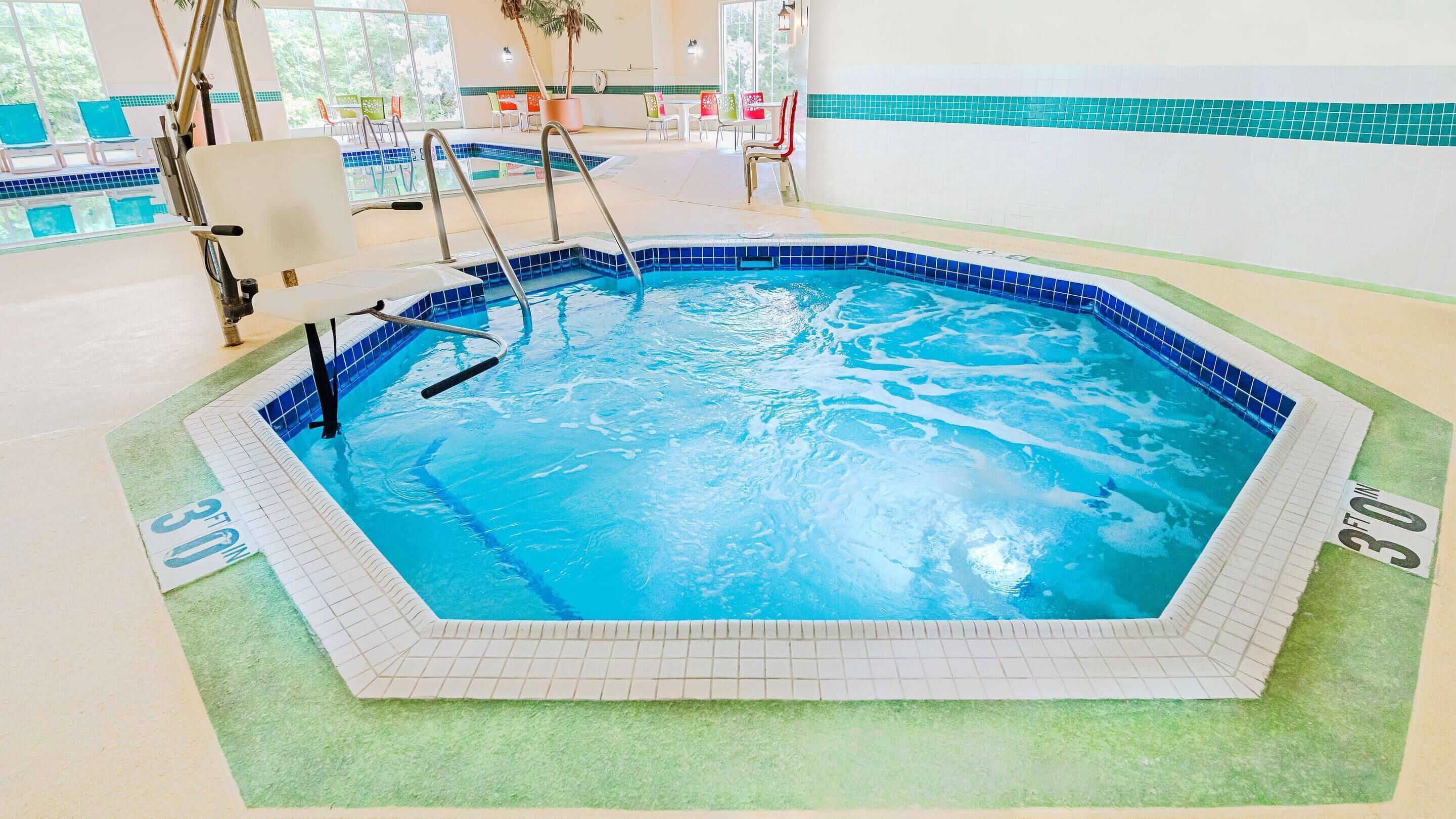 An indoor swimming pool with a tiled edge, a green mat surrounding the pool, and a view of the outside through large windows.