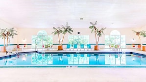 An indoor swimming pool with multiple lanes, surrounded by lounge chairs and potted palm trees.