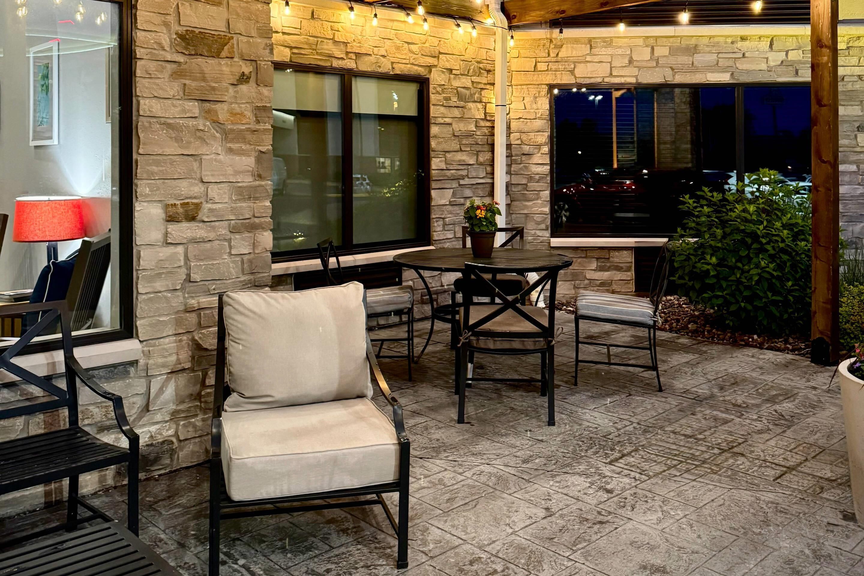 An outdoor patio area with stone walls, a table, chairs, and a lamp.