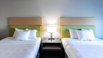 Habitación de hotel con dos camas individuales, cada una con ropa de cama y almohadas blancas, una mesita de noche con lámpara y un cabecero verde.