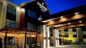 A hotel exterior with a covered outdoor seating area, stone pillars, and a sign reading "Country Inn & Suites by Bradisson."