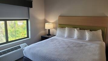 Een hotelkamer met een groot bed, een nachtkastje met een lamp en een raam met uitzicht op bomen.