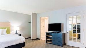 A hotel room with a bed, a TV on a dresser, a lamp, and a door leading to a bathroom.