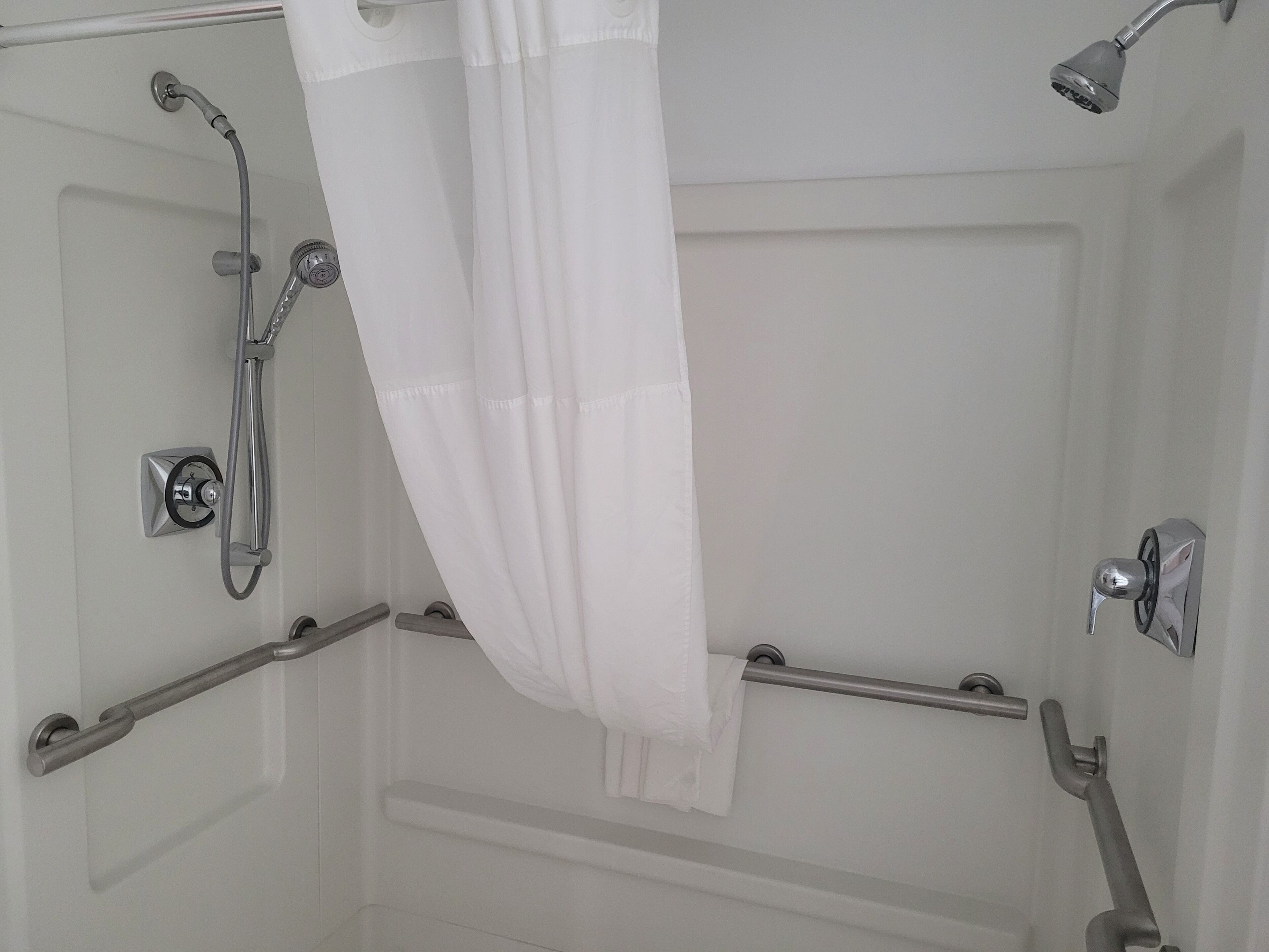 A shower area with a handheld showerhead, a wall-mounted faucet, and a grab bar.