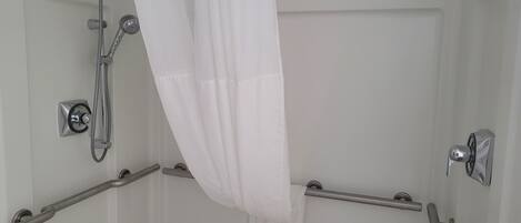 A shower area with a handheld showerhead, a wall-mounted faucet, and a grab bar.