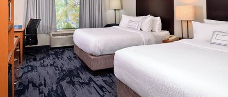 A hotel room with two beds, a desk, a chair, a lamp, and a window with curtains.