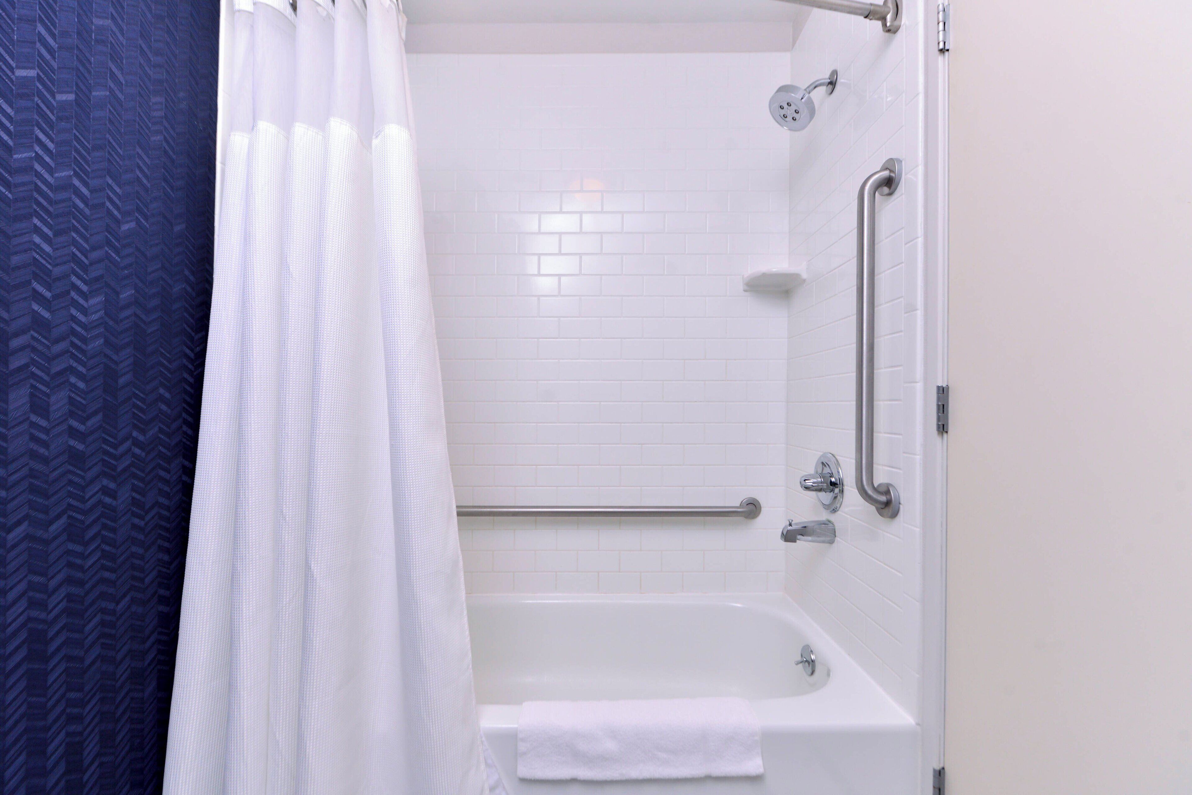 A bathroom with a white bathtub, a shower curtain, and a handrail.