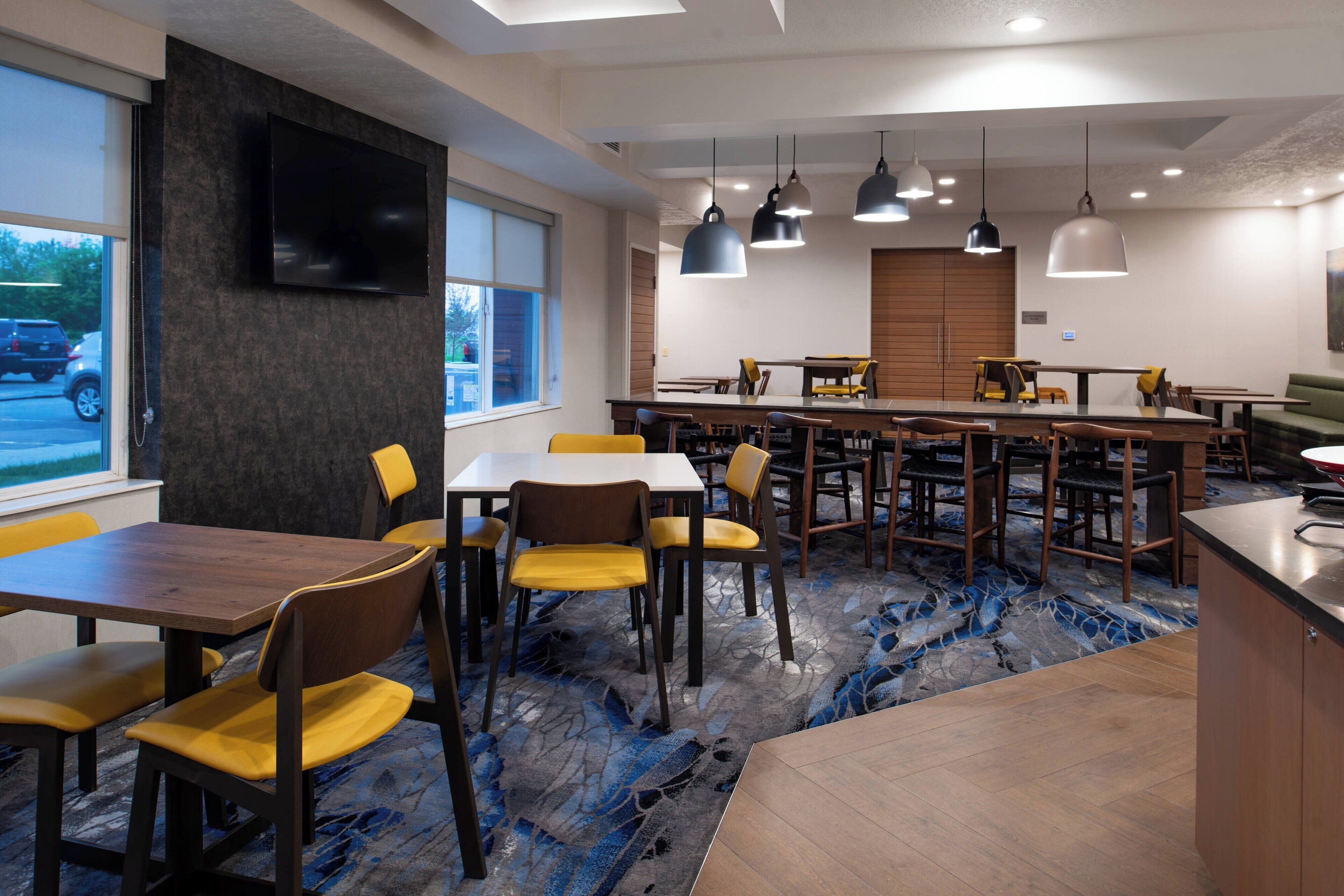A modern dining area with multiple tables and chairs, a bar counter, and a flat-screen TV mounted on the wall.