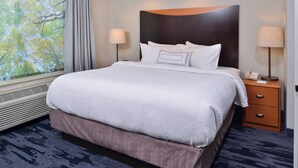 Habitación de hotel con una cama grande, dos mesitas de noche con lámparas, una ventana que da a vistas de árboles y un calentador instalado en la pared.