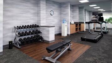 Un gimnasio con banco, mancuernas, cinta de correr y dispensador de agua.