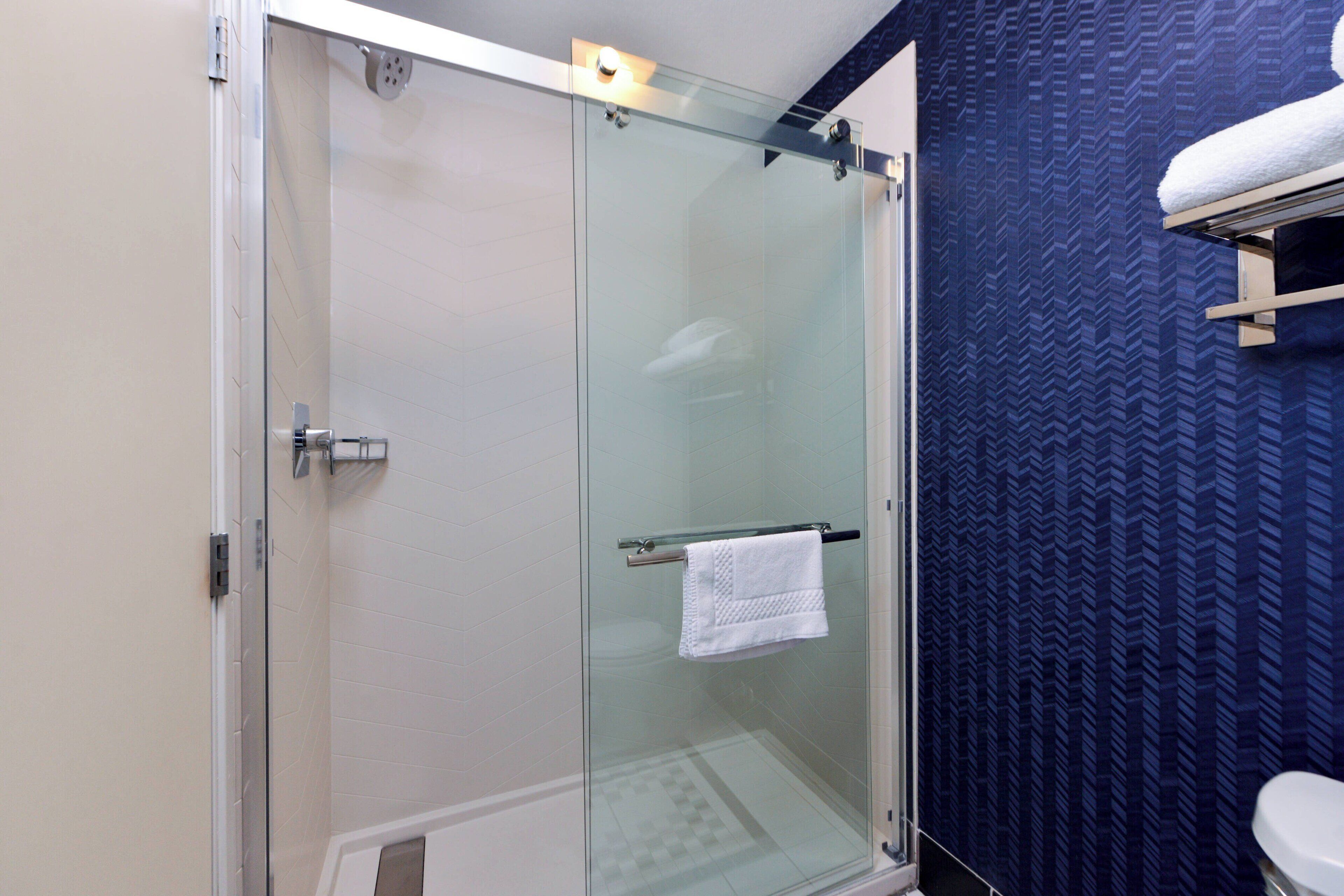 Eine begehbare, gläserne Dusche mit einem weißen Handtuch an einem Haken, einer weißen Toilette und einer Wand mit blauem Muster.