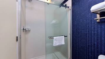 A glass-enclosed shower with a white towel hanging on a rack, a white toilet, and a blue patterned wall.