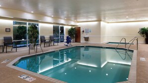 Una piscina interior con agua cristalina, rodeada de sillones de descanso y plantas en macetas.