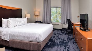 Habitación de hotel con una cama grande, un escritorio con computadora, televisor y ventana con cortinas.