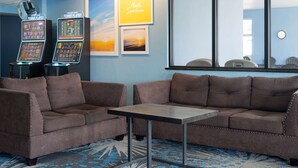 A room with two brown sofas, a small table, and two arcade machines. There are framed pictures on the wall and a window with a view. - Days Inn by Wyndham Neenah (Neenah)