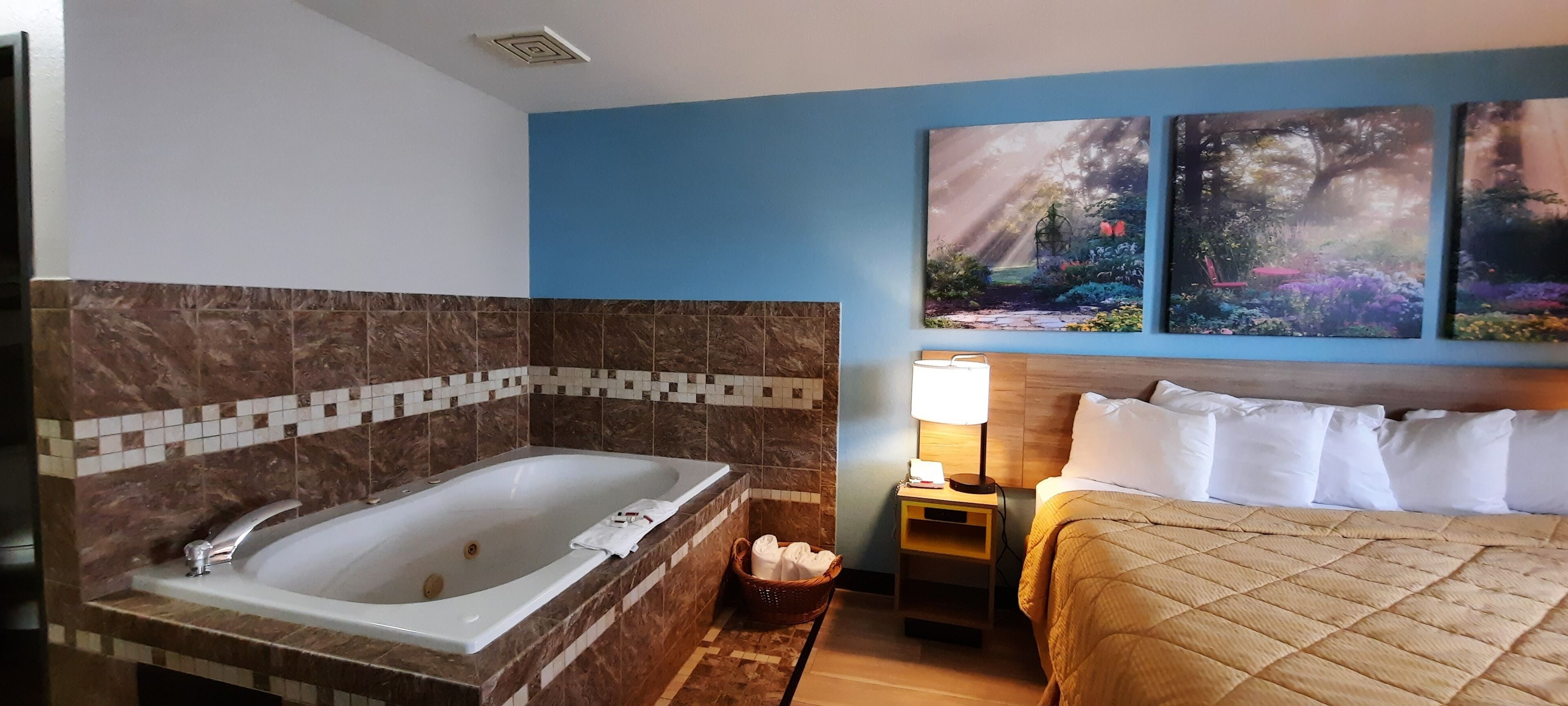 A hotel room with a large bathtub, a bed with white bedding, and two wall-mounted paintings.