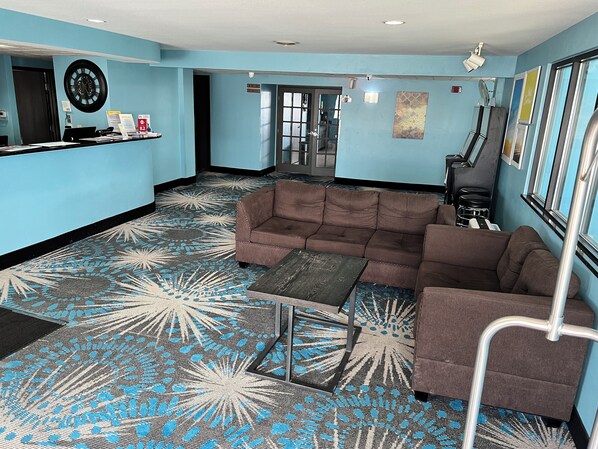 A lobby with a patterned carpet, a brown sofa, a small table, and a reception desk. - Days Inn by Wyndham Neenah (Neenah)