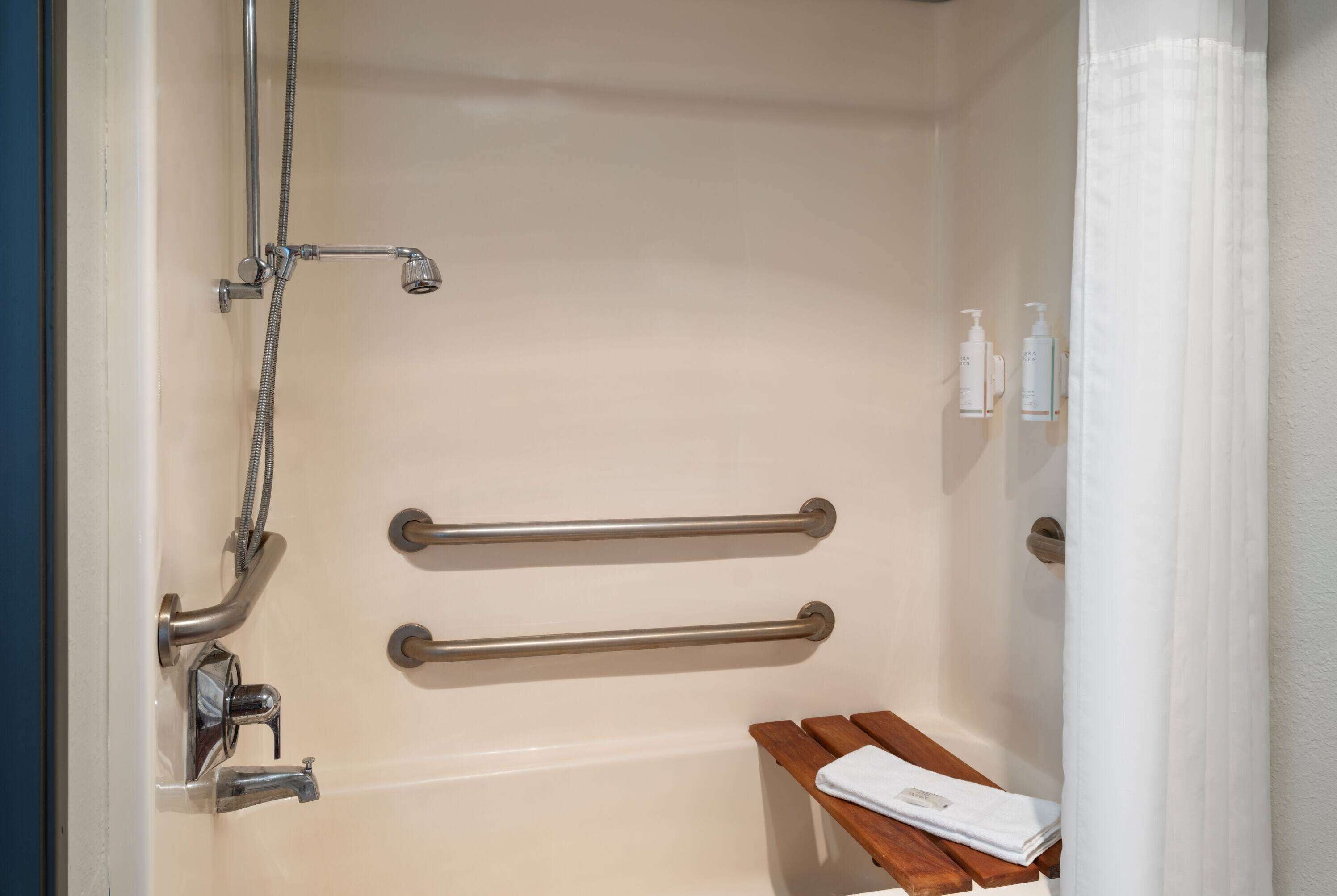 A bathroom with a shower, grab bars, a bench, and toiletries.