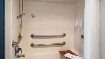 A bathroom with a shower, grab bars, a bench, and toiletries.