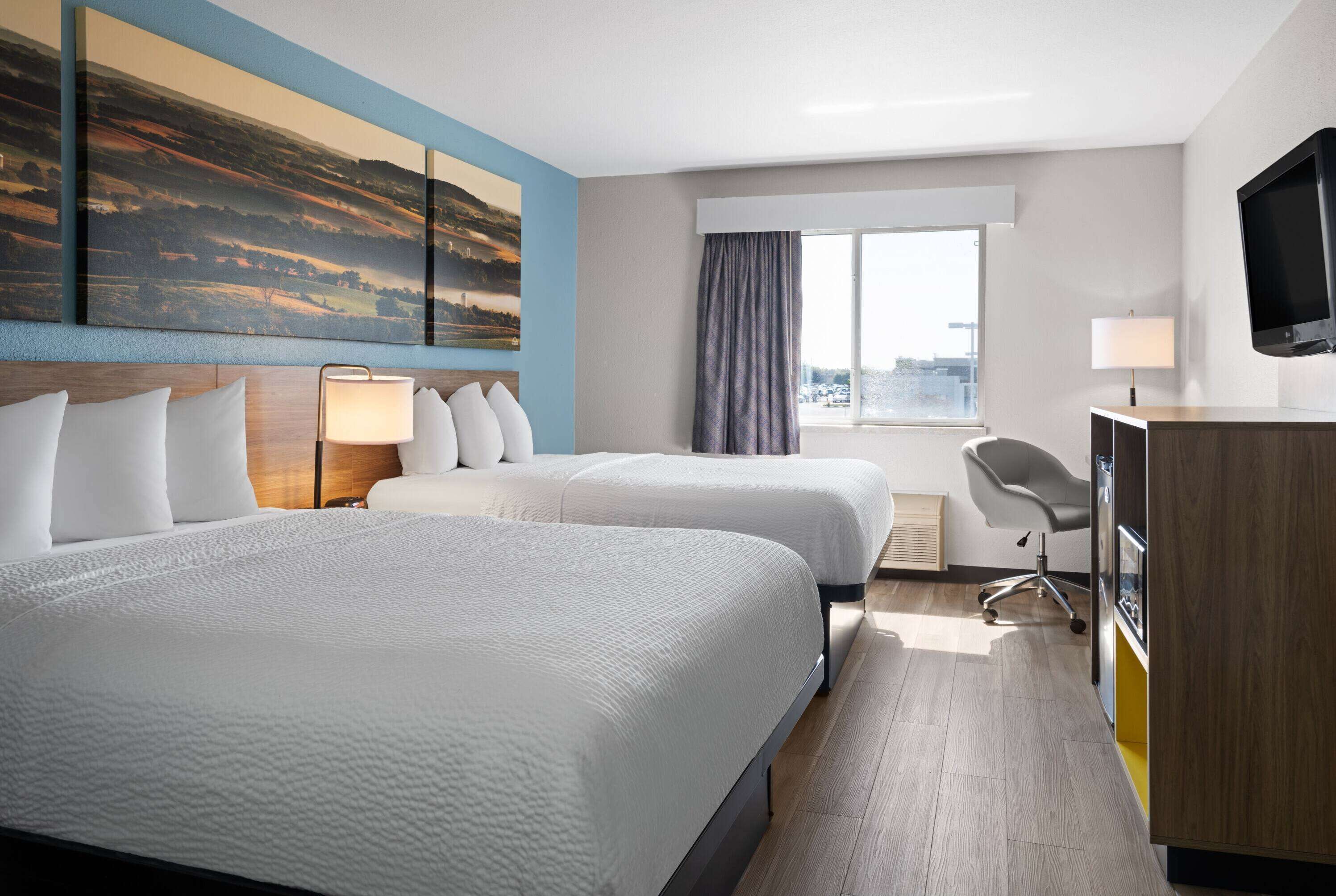 A hotel room with two beds, a desk, a chair, a TV, and a large window.