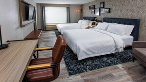 Habitación de hotel con dos camas, un escritorio, una silla, un televisor y un ventanal grande.