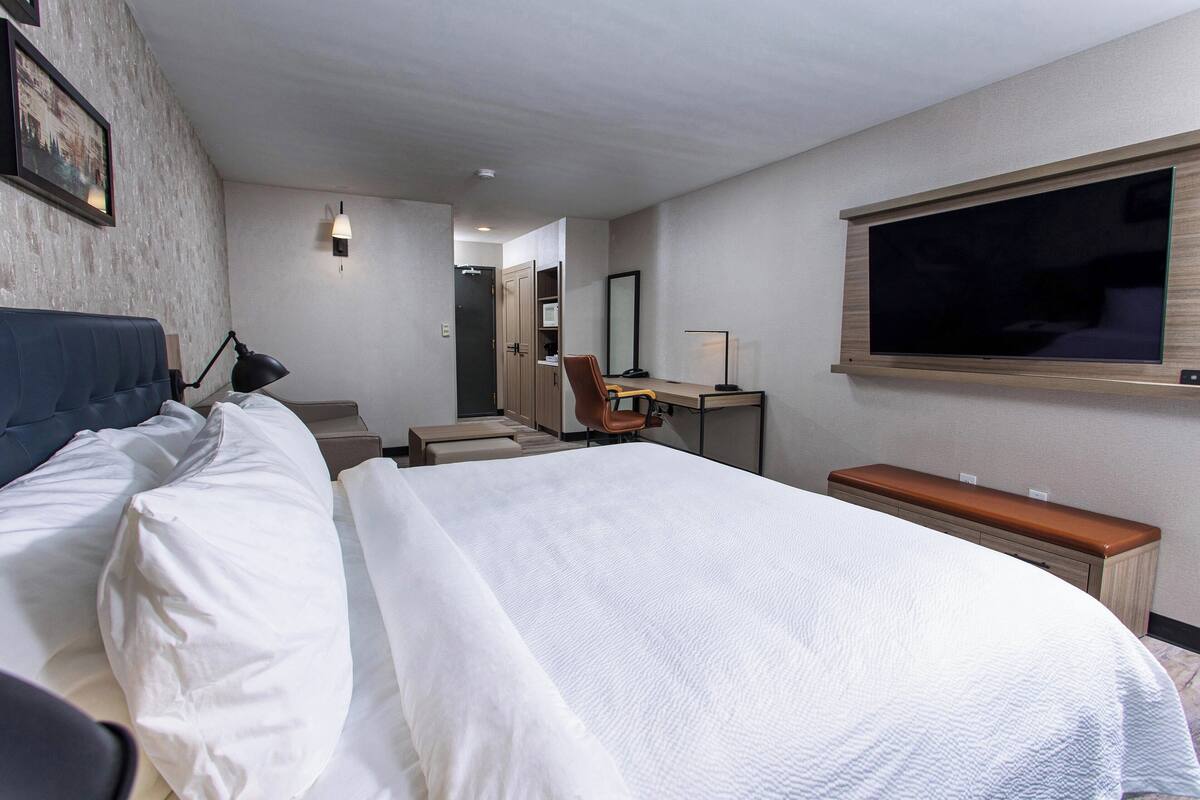 A hotel room with a large bed, a desk with a chair, a TV, and a wardrobe.