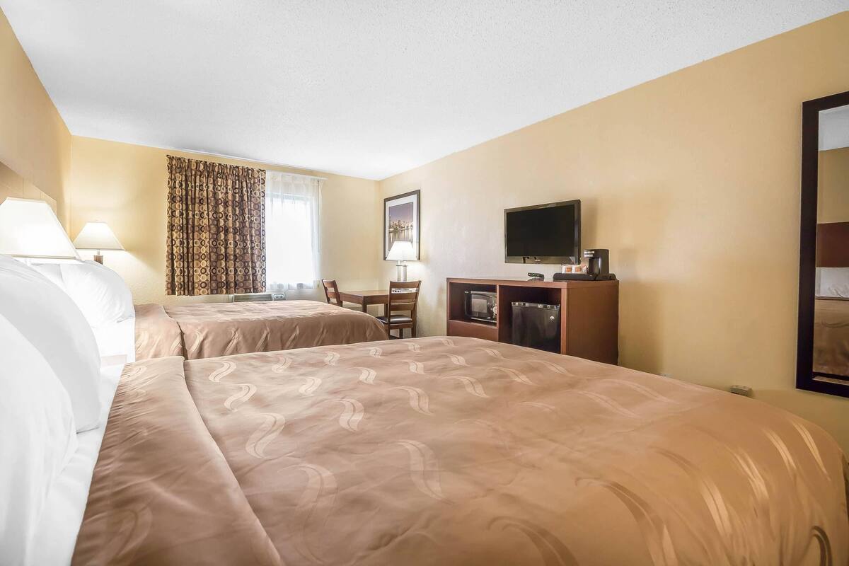 A hotel room with two beds, a desk with a chair, a television, and a minibar.