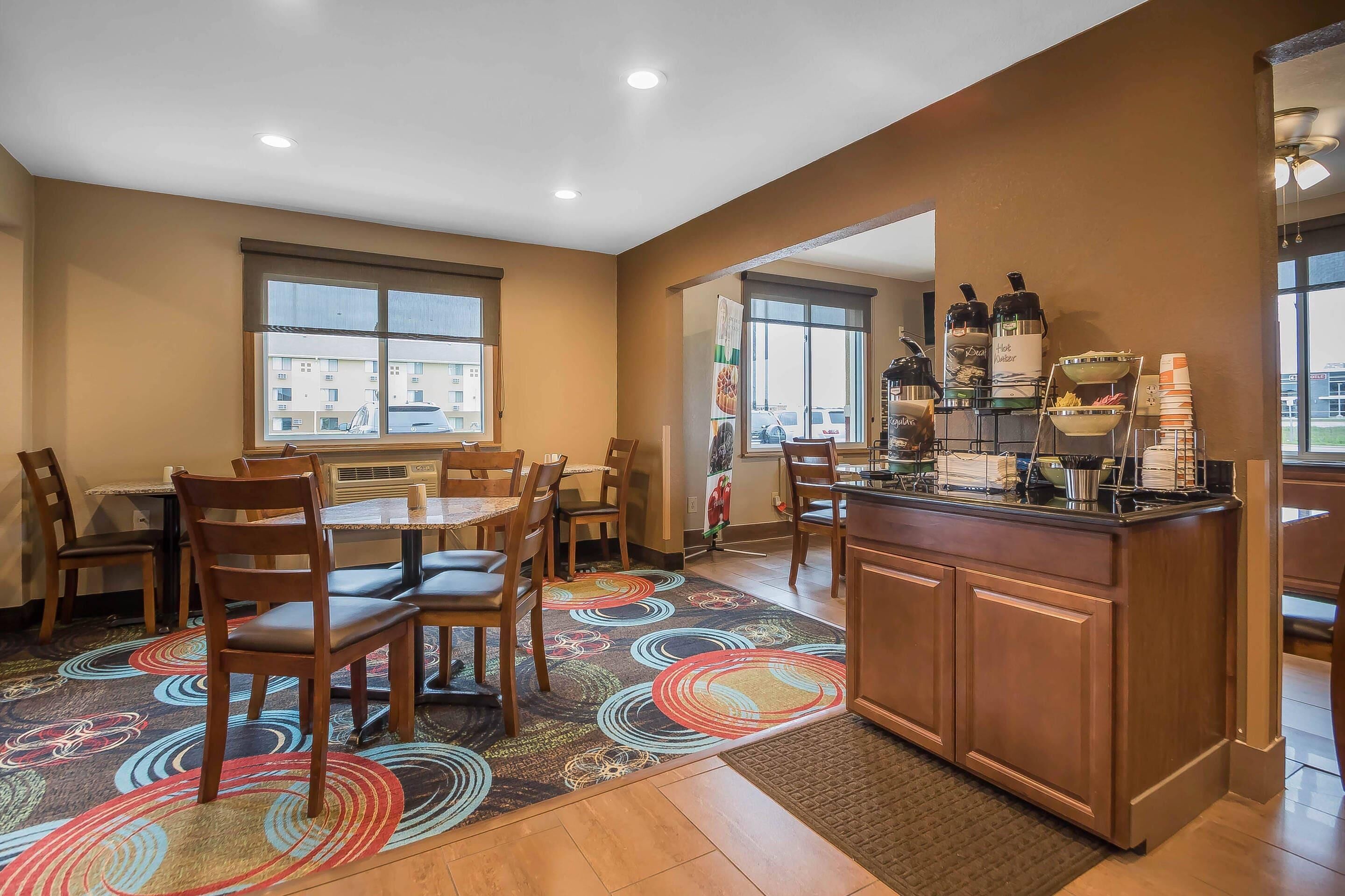 A hotel room with a dining area, a kitchen counter with beverages, and a view of the outside.