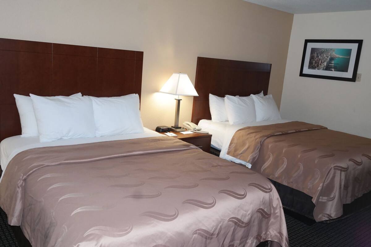 A hotel room with two beds, a nightstand with a lamp, a phone, and a framed picture on the wall.