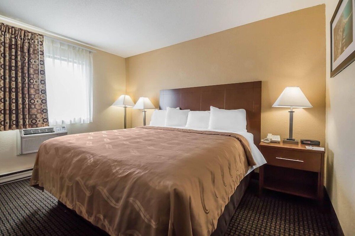 A hotel room with a large bed, two bedside lamps, a nightstand, and a window with curtains.