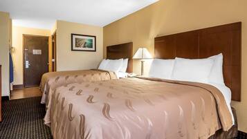 Habitació d'hotel amb dos llits, un amb capçalera de fusta, un quadre encarregolat a la paret i una làmpada a la tauleta de nit.