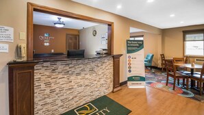A hotel reception area with a stone wall, a reception desk, a clock, and a dining area with chairs and a table.