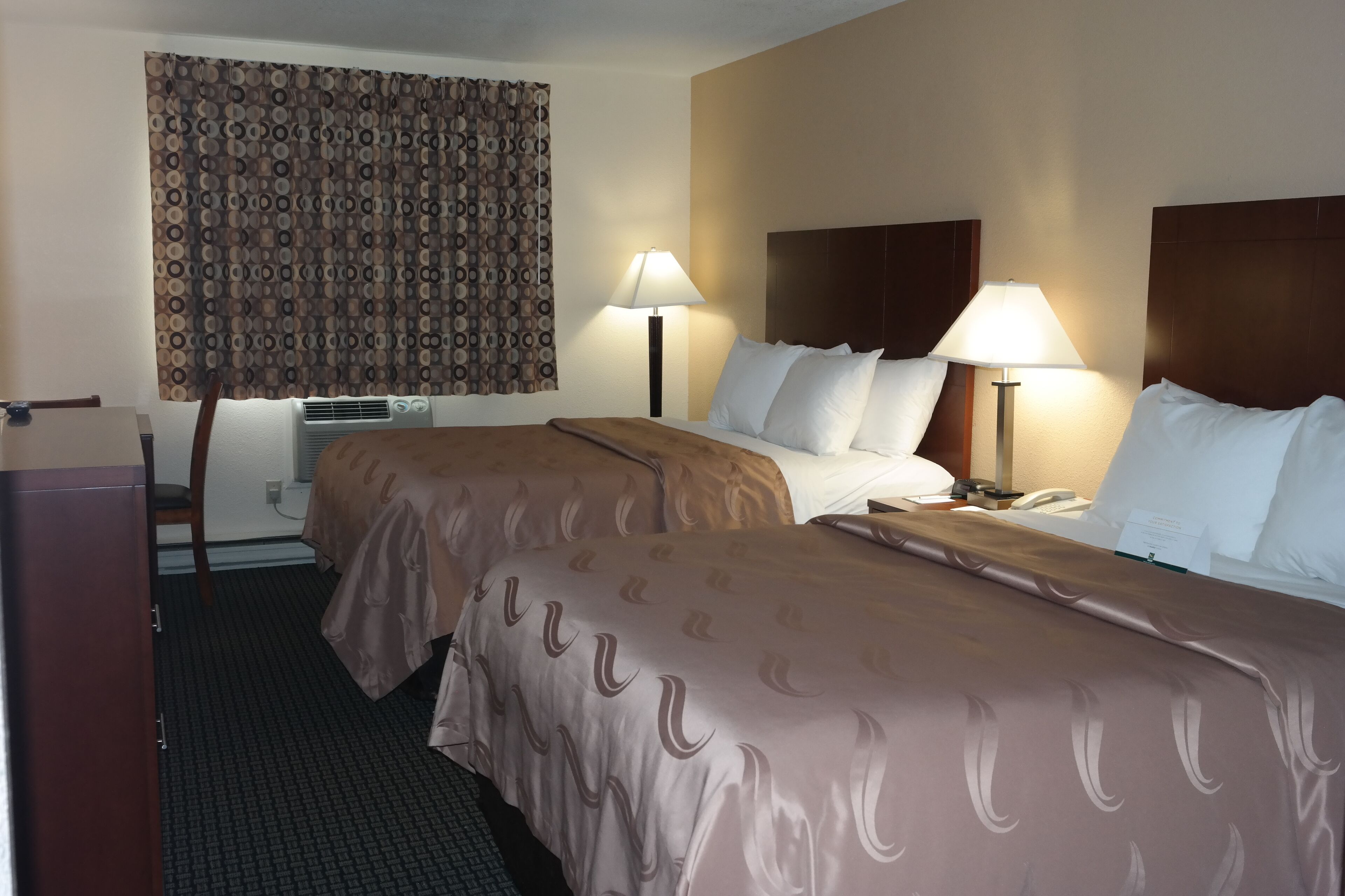 A hotel room with two beds, a desk, a chair, a lamp, and a curtain.